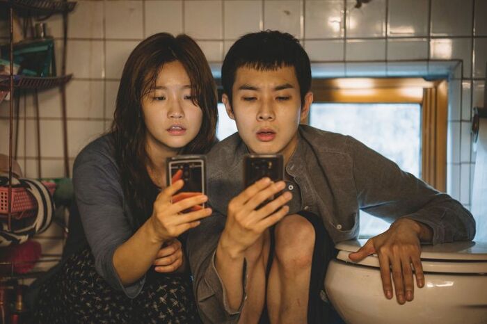 Still image of young couple holding phones from the Korean film Parasite